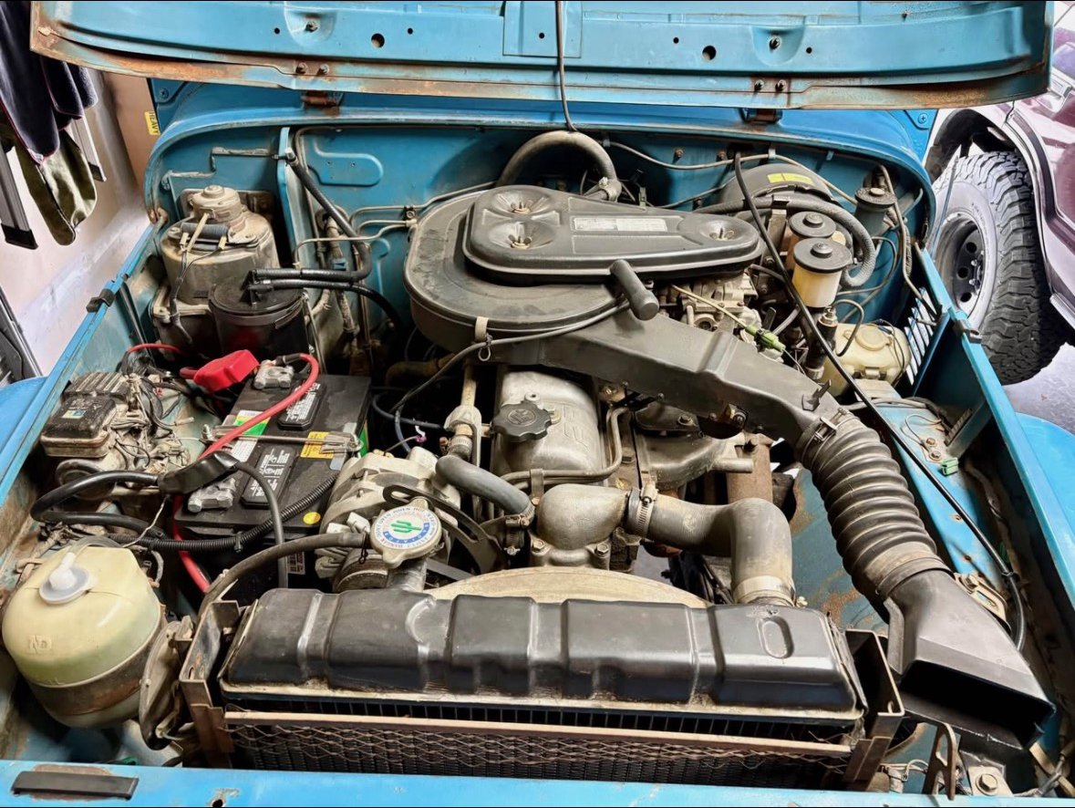 The FJ40 engine bay as bought: original inline-six, battery, and fifty years of hoses and wiring