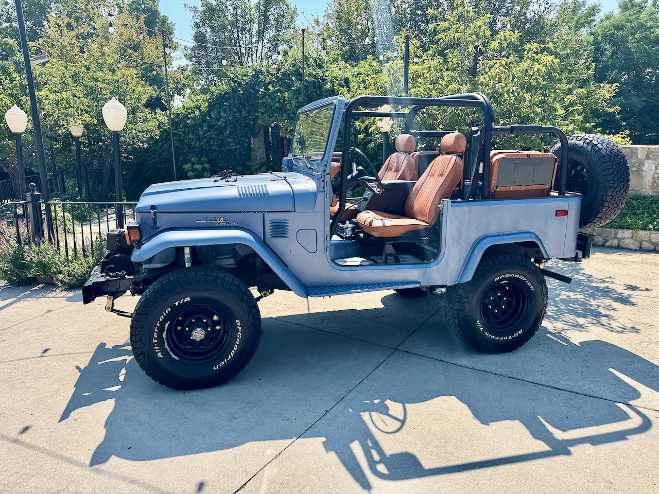 The finished FJ40 in profile: roll cage, saddle-brown seats, rear-mounted spare, parked in the sun