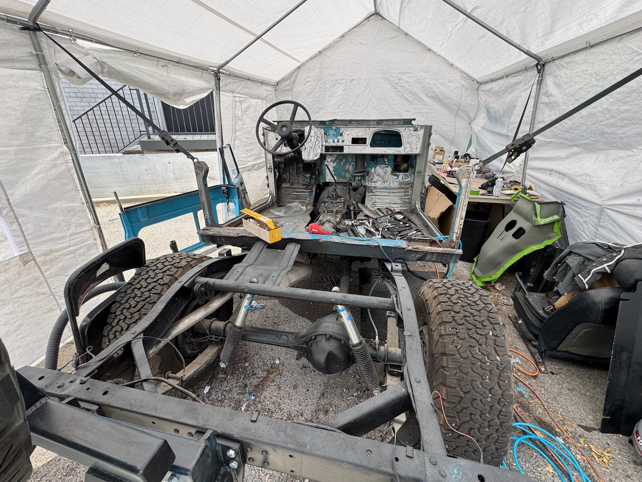 The 1977 FJ40 under a tent with the body lifted off the frame, rolling chassis in front, tools and parts everywhere