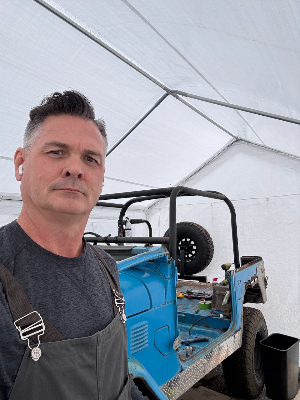 Jarad in overalls in the tent with the stripped FJ40 body behind him