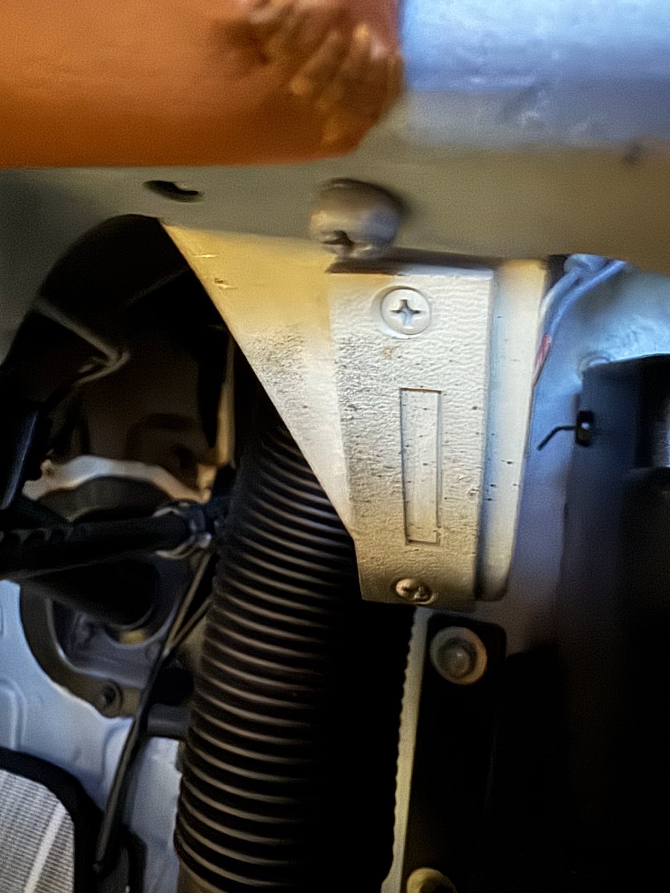 Close-up of an unidentified stamped-metal bracket in the FJ40 engine bay, next to a corrugated hose